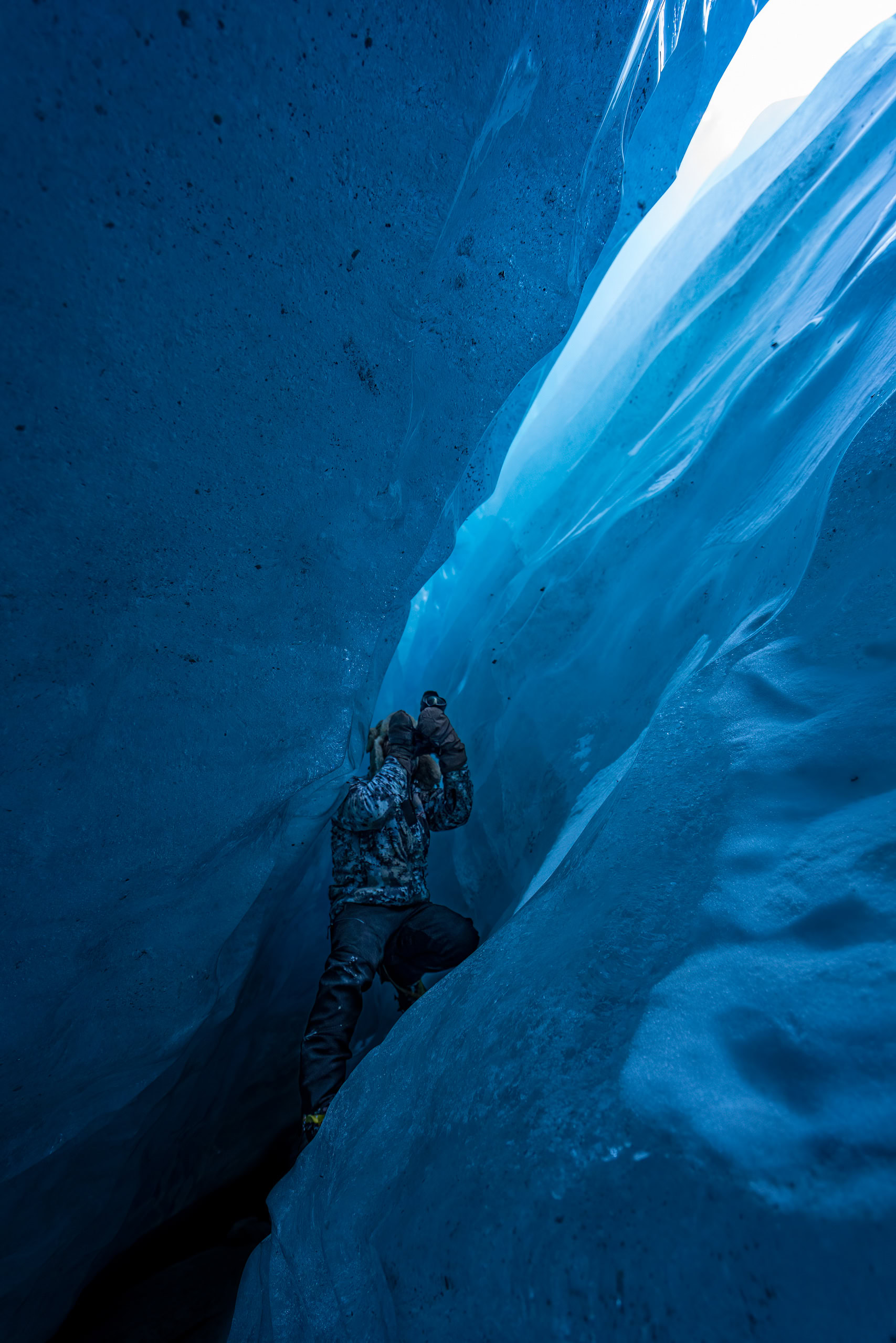 Eis-Spezialist beim Klettern in einer blau schimmernden Gletscherhöhle, die Temperatur hält die Eisformationen intact. Perfektes Bild für Naturfotografie, Abenteuer und alpine Expeditionen.