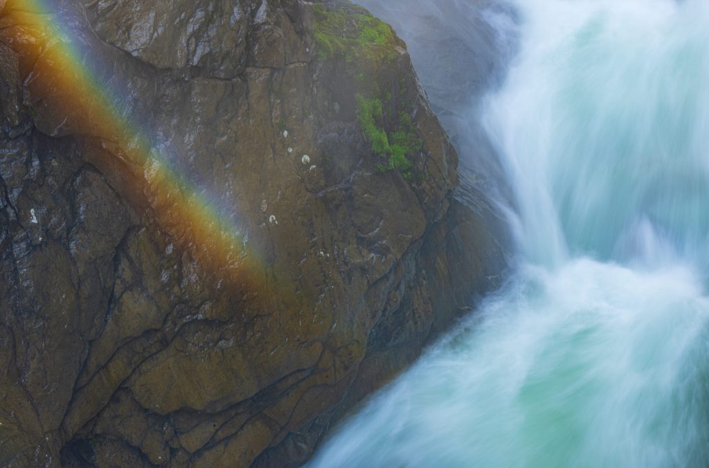 Farbenfroher Regenbogen an rauer Felsenwand bei Fluss in Tirol, Österreich.