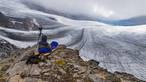 1. Spektakulärer Blick auf Gletscher in den Alpen, Fotograf beim Fotografieren der Eislandschaft auf einer felsigen Klippe, Outdoor-Abenteuer, Natur, Berglandschaft, nachhaltige Fotografie.
