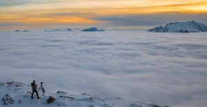 1. Hochalpiner Fotograf bei Sonnenuntergang mit Blick auf Wolkenmeer und schneebedeckte Berge in Österreich.
