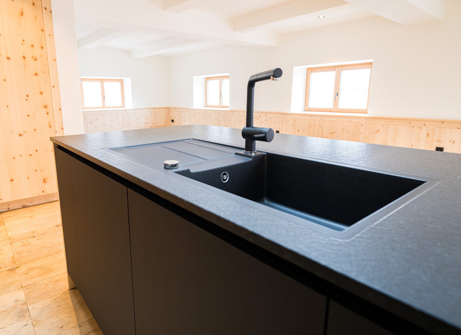 Moderner schwarze Küchenspüle mit Wasserhahn in hellem Holzdesign, typisch für elegante Küchen von Philipp Egger, bekannt für nachhaltige und hochwertige Raumgestaltung.