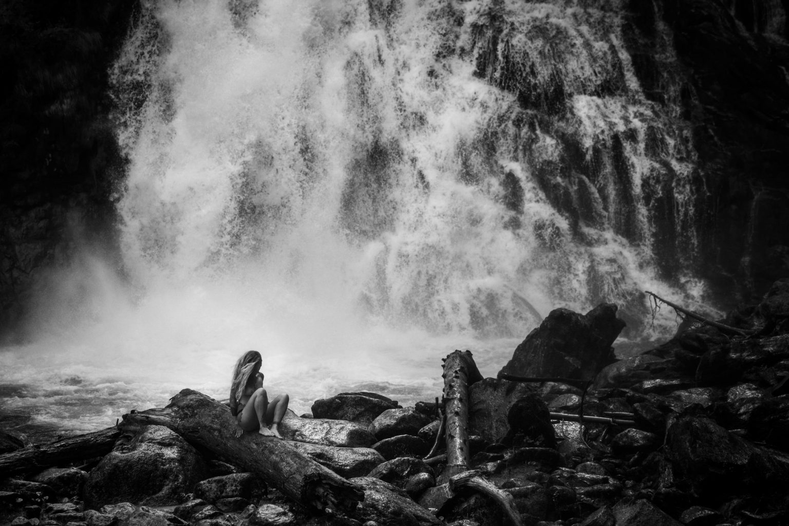 Starke Wasserfälle in Schwarz-Weiß, Naturaufnahme, ruhige Szene mit Frau auf Felsen, beeindruckende Landschaft, Outdoor-Abenteuer, Naturfotografie, Entspannung in der Natur, perfekte Kulisse für Naturliebhaber und Fotografie-Enthusiasten.