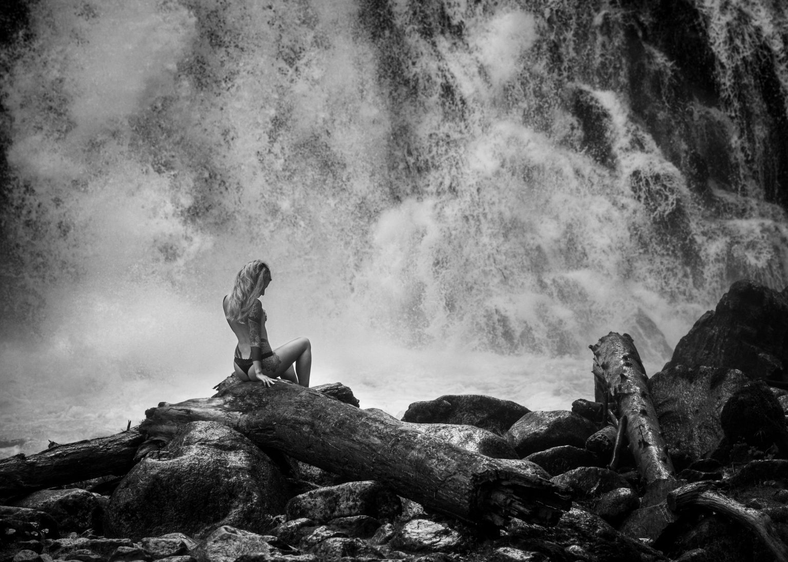 Ladylike Frau sitzt auf Steinen vor Wasserfall in Natur, Schwarz-Weißaufnahme, Entspannung, Naturerlebnis, Outdoor-Aktivität, kraftvolle Wasserlandschaft, inspirierend, Freiheit, Abenteuer, Meditation, Selbstfindung, Meditation, Inspiration, Naturfotografie.
