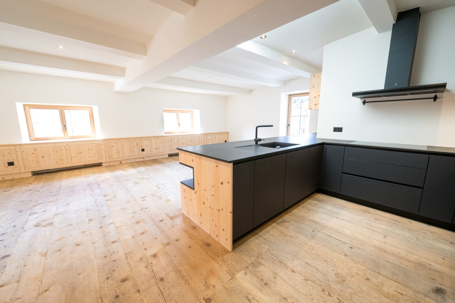 Moderner, minimalistischer Küchenbereich mit schwarzen Schränken, Holzdetails und viel natürlichem Licht, ideal für elegante, funktionale Wohnräume nach dem Optima-Design.